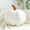 A white pumpkin plush pillow with a brown stem rests on a white knitted fabric.