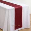 Elegant satin table runner in deep burgundy laid across a white tablecloth.