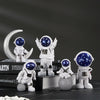 A collection of handcrafted astronaut figurines in white and blue, including a full figure, a helmet, and a small sphere.
