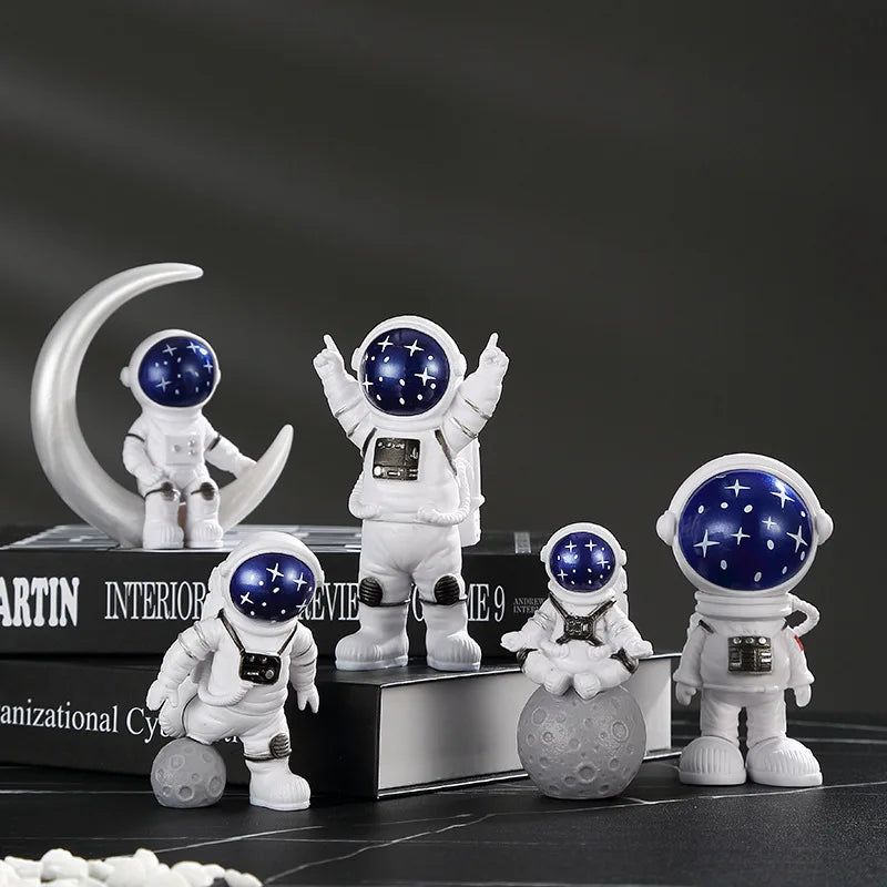A collection of handcrafted astronaut figurines in white and blue, including a full figure, a helmet, and a small sphere.