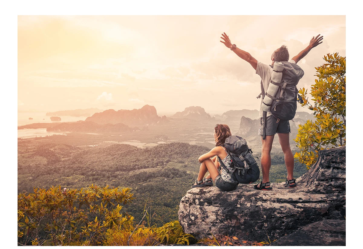 A person stands on a rocky cliff overlooking a vast landscape with warm sunlight, holding a paracord rope.