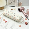 A pink quilted cotton hair dryer storage bag with a handle resting on a white cloth next to a framed picture.