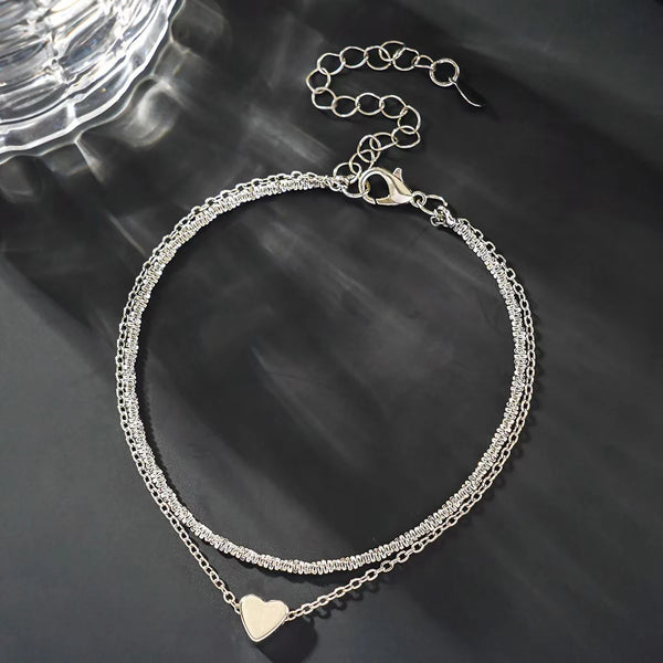 Un délicat anklet en argent à chaîne avec un design superposé et un charm à cœur.