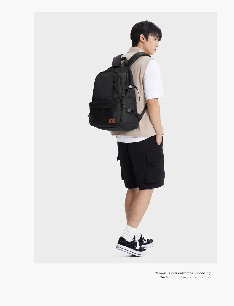 A young man wearing a tan shirt and black shorts carries an olive green laptop backpack.