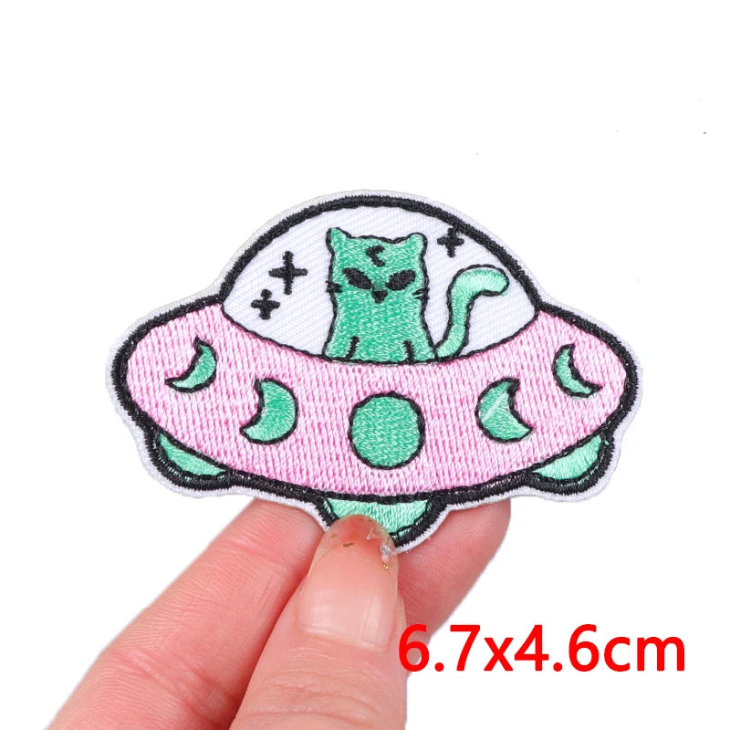 A pink and green embroidery patch featuring a cartoon cat inside a stylized, round design.