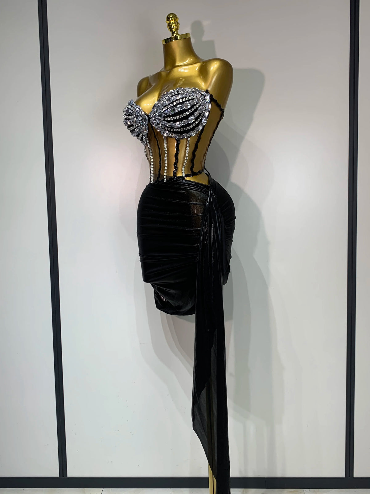 A mannequin displays a sparkly two-piece party outfit featuring a sheer top and a black draped skirt.
