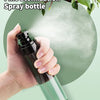 A hand is holding a dark glass spray bottle with a fine mist, set against a light green background.