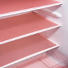 A close-up view of a pink waterproof refrigerator liner mat with white edges inside a shelf.