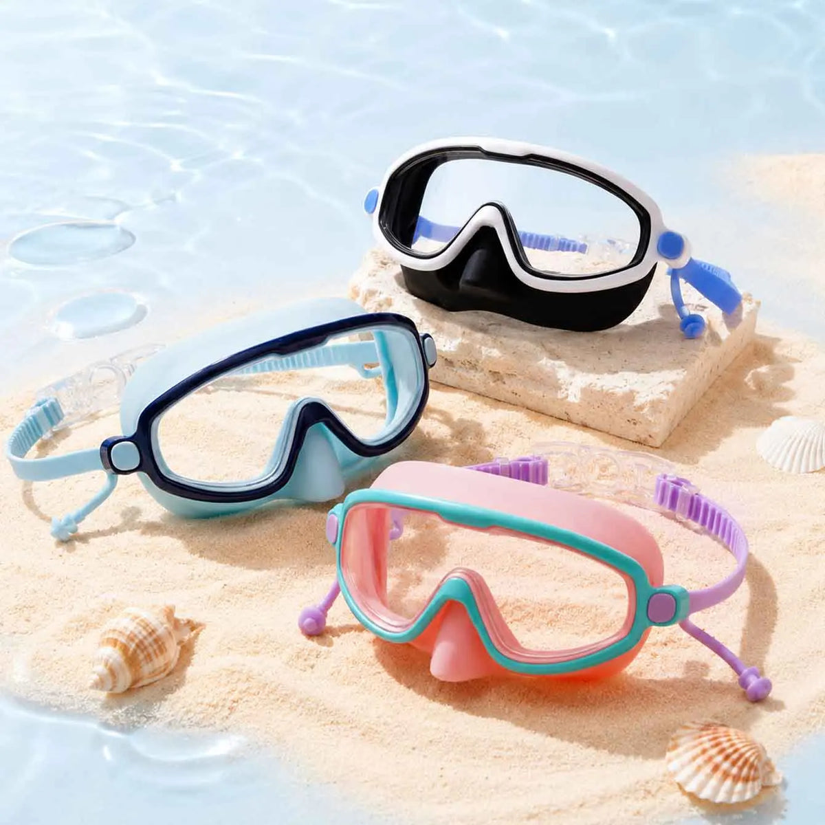 Un ensemble de lunettes de natation anti-buée à large vue en noir, bleu et rose posées sur du sable clair avec des coquillage