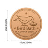 A round copper disk bird bath with a silhouette of a bird on it, designed for garden water.