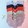 A stack of three soft cotton baby bibs in blue, navy, and rust colors with ruffle trim.