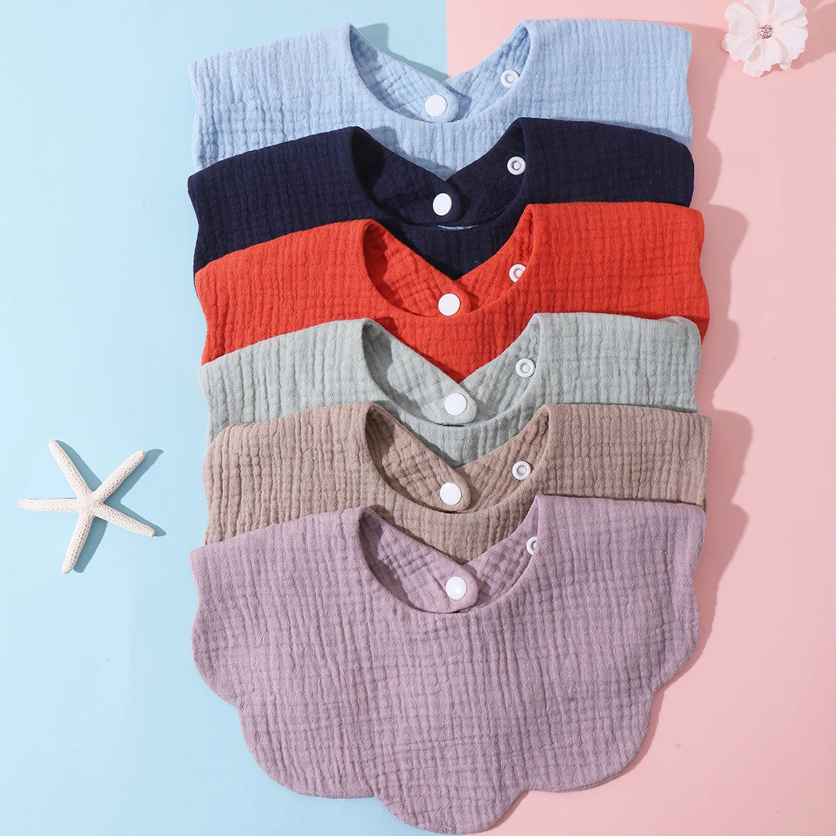A stack of three soft cotton baby bibs in blue, navy, and rust colors with ruffle trim.