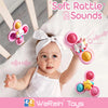 A baby is playing with a pink and yellow soft rattle toy designed to make gentle sounds.