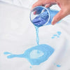 A hand pours blue liquid from a glass into a puddle on white fabric, demonstrating the waterproof fitted mattress protector.