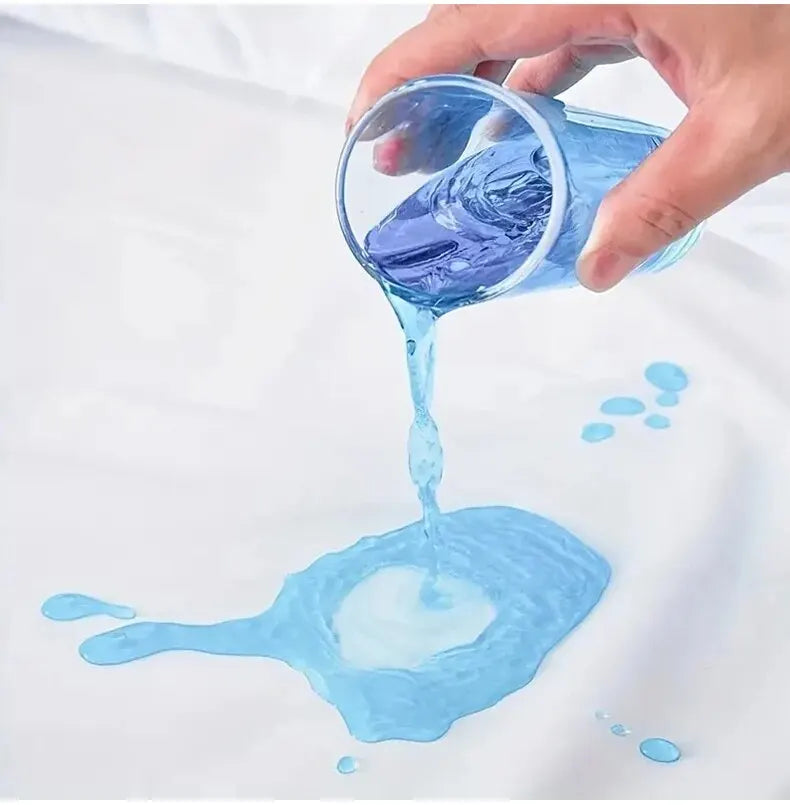 A hand pours blue liquid from a glass into a puddle on white fabric, demonstrating the waterproof fitted mattress protector.