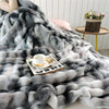 A fluffy gradient fleece throw blanket in shades of gray and white draped over a surface.