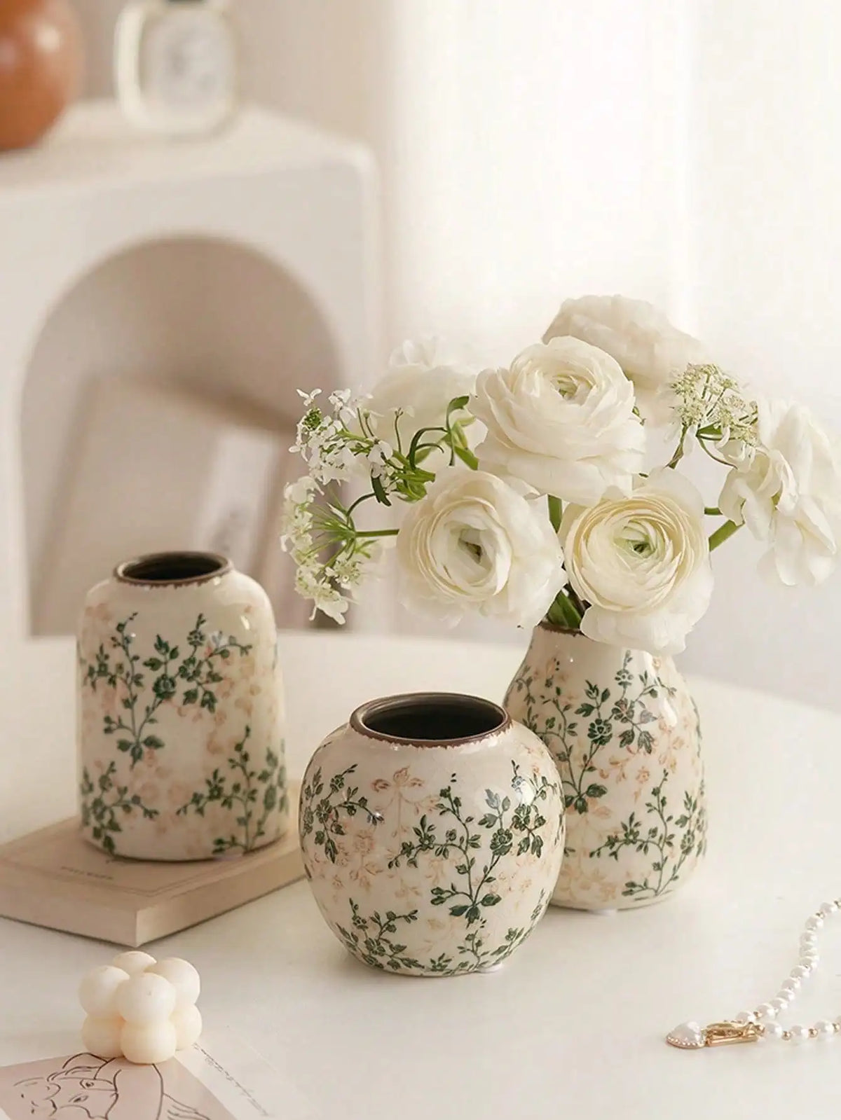 Weiße Keramikvase mit grünen Blumenmustern hält einen Strauß weißer Rosen und Babyblumen.