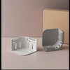 A light gray plastic bed sheet holder with multiple clips is shown next to a brown cardboard box.