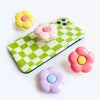 A foldable phone grip stand featuring colorful, squishy flower-shaped silicone grips in yellow, pink, and purple.