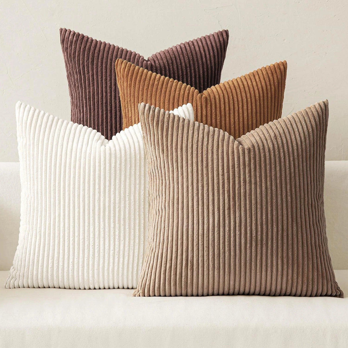 A grouping of four textured throw pillows in shades of brown, beige, and cream corduroy fabric.
