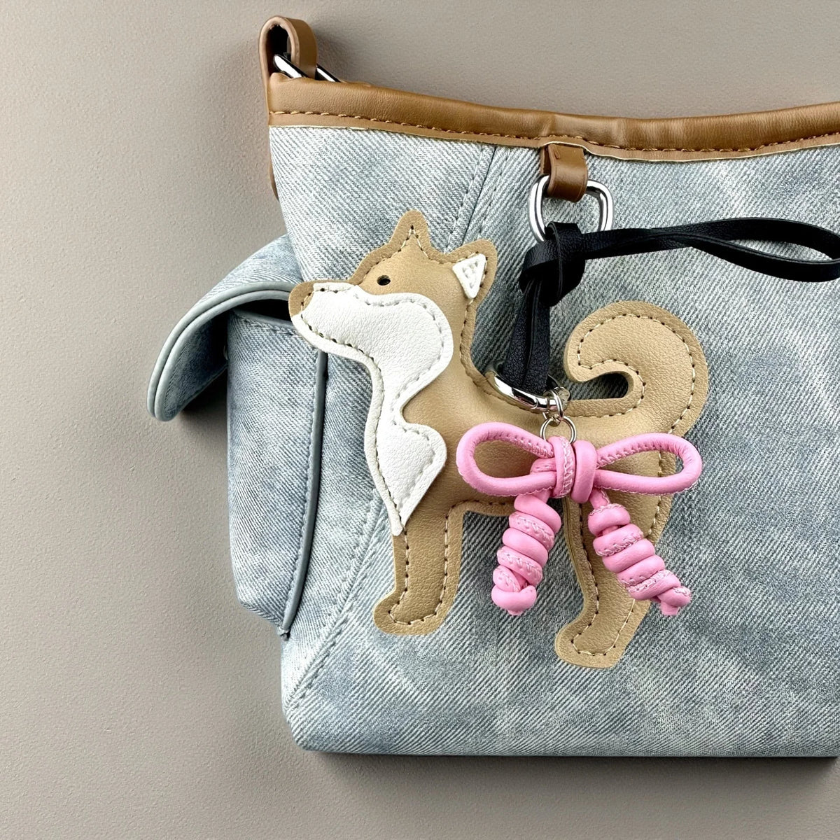 A light blue denim fabric bag featuring a tan Shiba Inu leather charm with a pink braided bow.