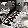 A collection of black and white patterned mats, including a long happy rug and decorative pillows, displayed on a floor.