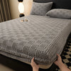 A gray knitted mattress cover with an elastic edge is shown on a bed, next to a lamp.