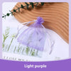 A purple organza drawstring gift bag tied with a ribbon, displayed on a wooden surface next to dried floral elements.