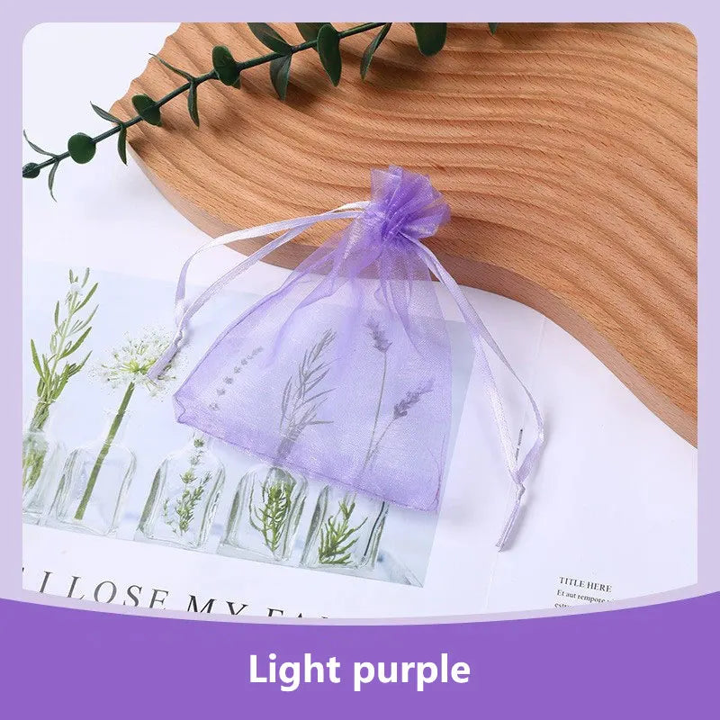 A purple organza drawstring gift bag tied with a ribbon, displayed on a wooden surface next to dried floral elements.