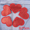 A set of five red glitter heart iron-on patches placed on a denim fabric background.