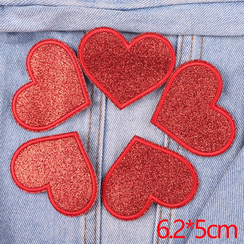 A set of five red glitter heart iron-on patches placed on a denim fabric background.