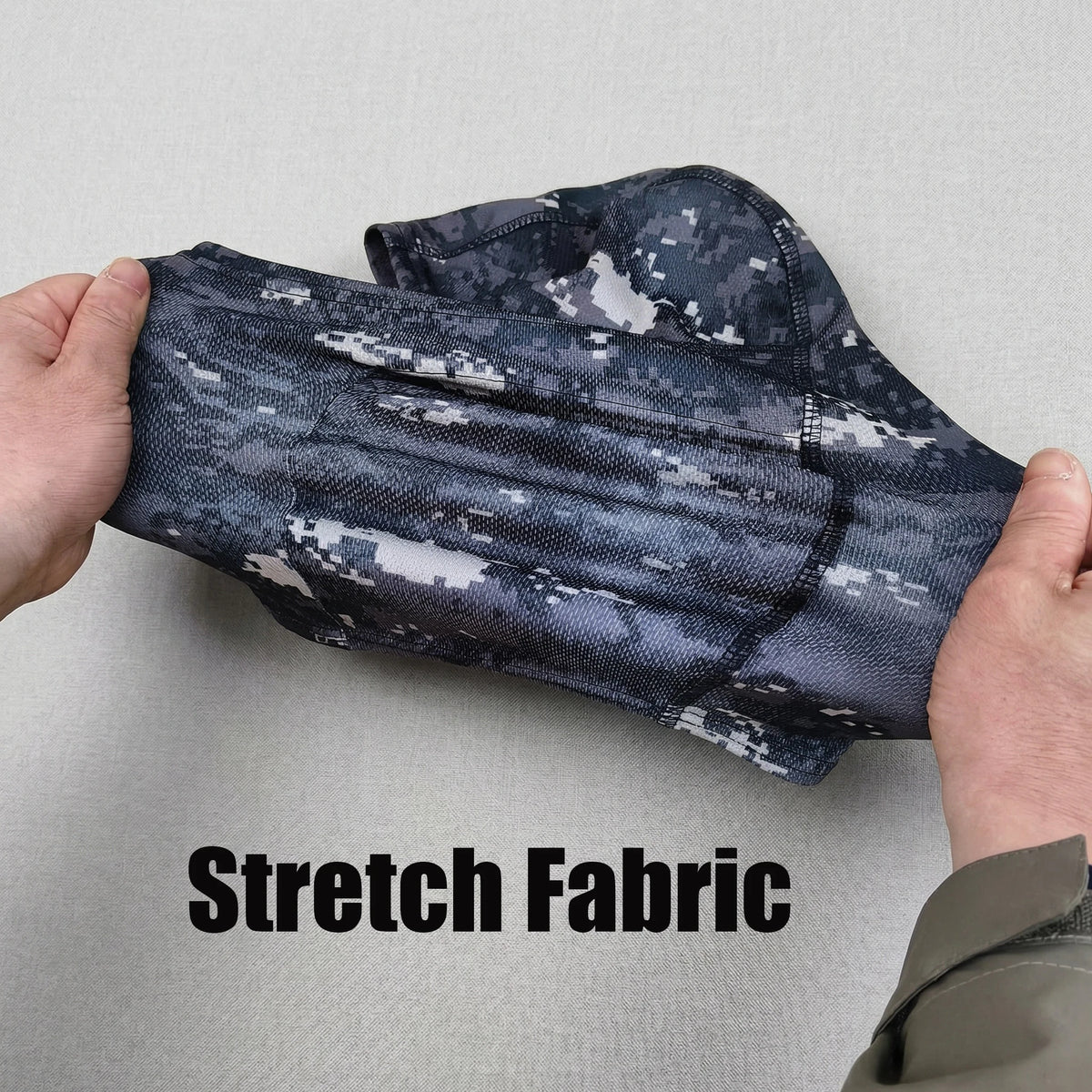 A hand is holding a dark gray camouflage stretch fabric material.