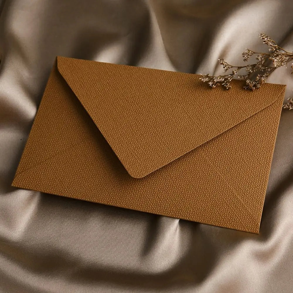 A kraft brown envelope with a triangular flap and gold sealing wax stickers resting on draped fabric.