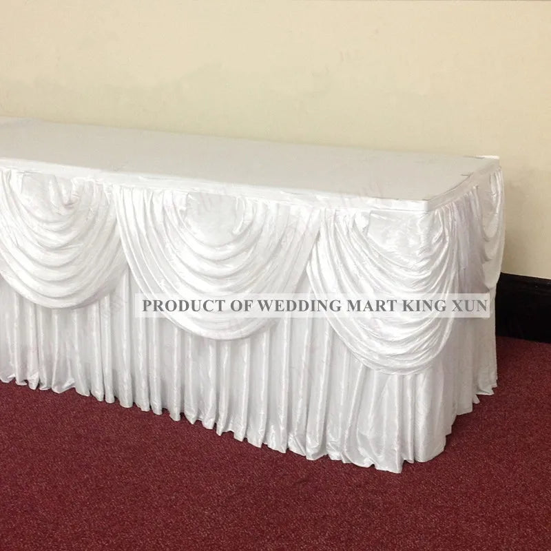 White ice silk table skirt with ruffled fabric and matching top swag displayed on a dark red surface.