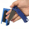 A hand holds a compact folding knife with a dark blade and blue nylon fiber handle.