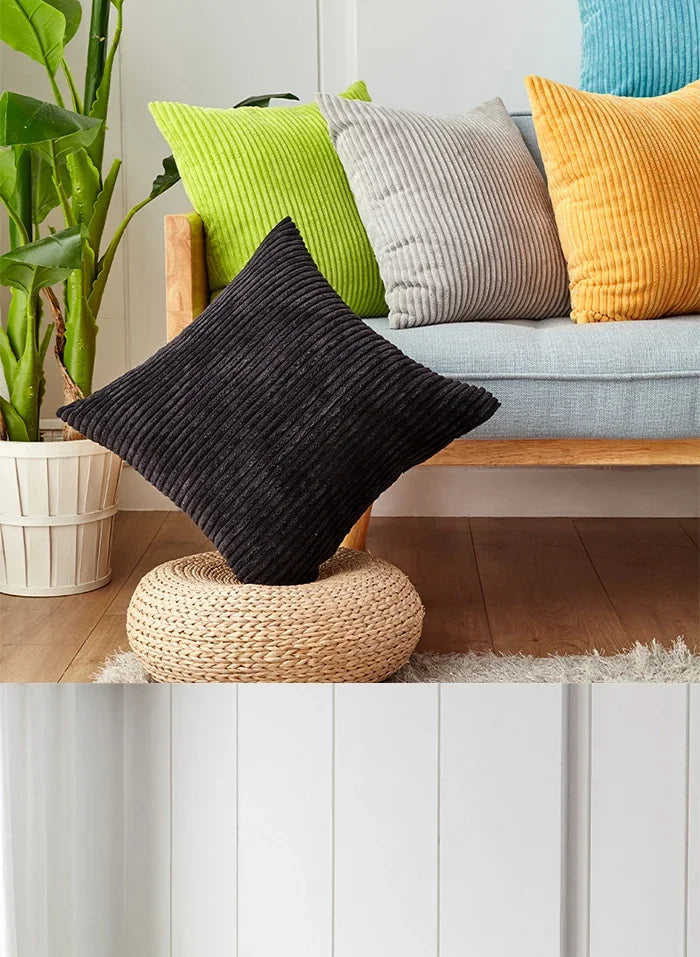 A set of striped velvet corduroy cushion covers in black, gray, lime green, and mustard yellow displayed on a wooden bench.