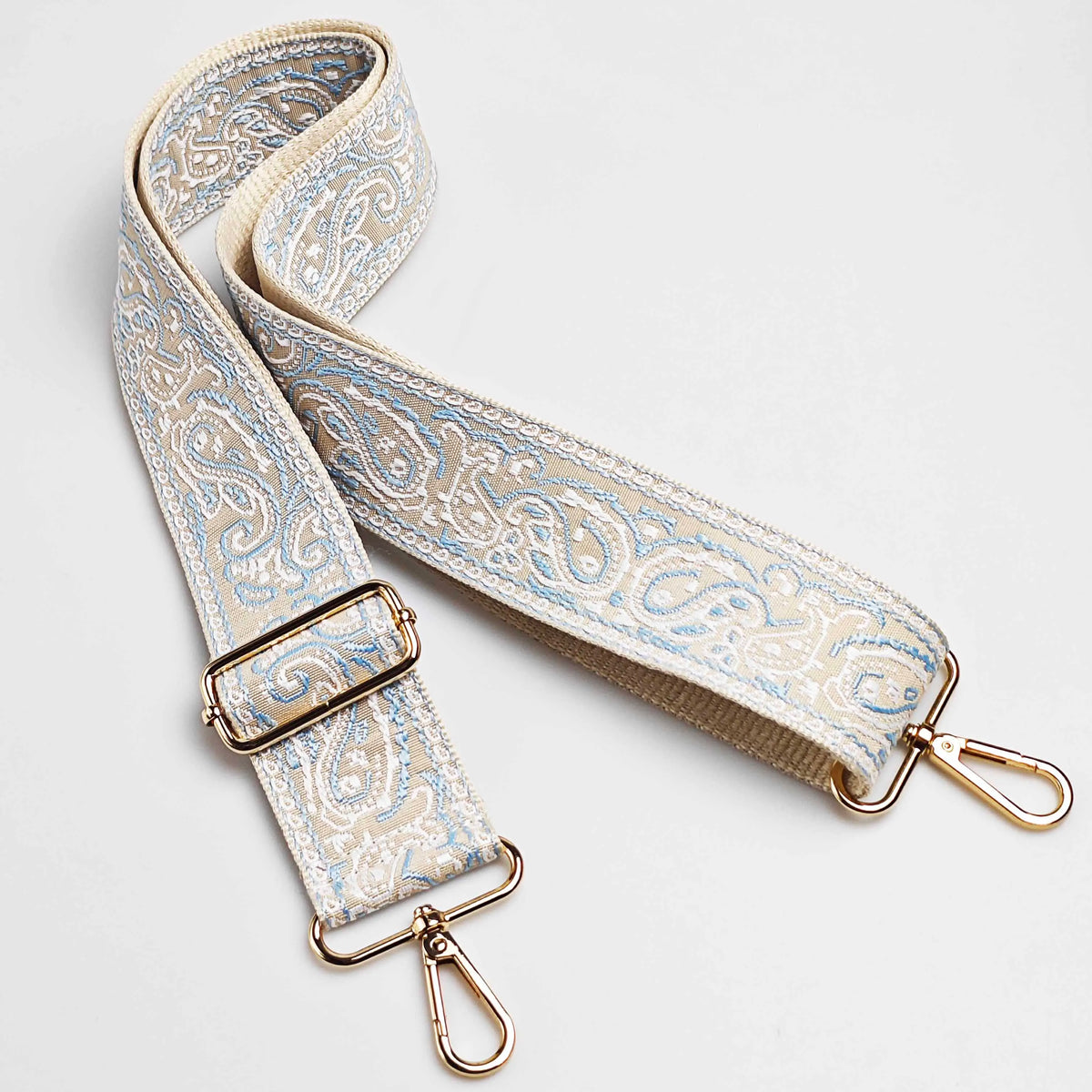 A beige and blue paisley jacquard bag strap with gold hardware.
