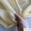 A hand is gently folding a piece of pale yellow silk chiffon fabric.