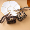 A leopard print PU leather keychain mini wallet with gold hardware resting on a white tile.