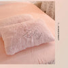 A pink fluffy pillow resting on a light pink bed with a white patterned sheet.