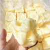 A hand holds a block of realistic cheese squishy stress relief fidget toy surrounded by other yellow cheese blocks.