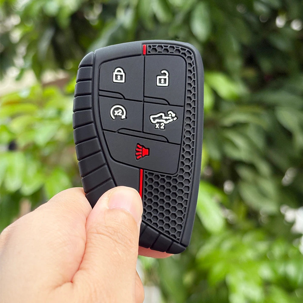 A hand holds a black silicone key fob cover with various buttons and a red indicator light.