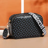Black compact crossbody bag with a patterned print and gold hardware resting on a light surface.