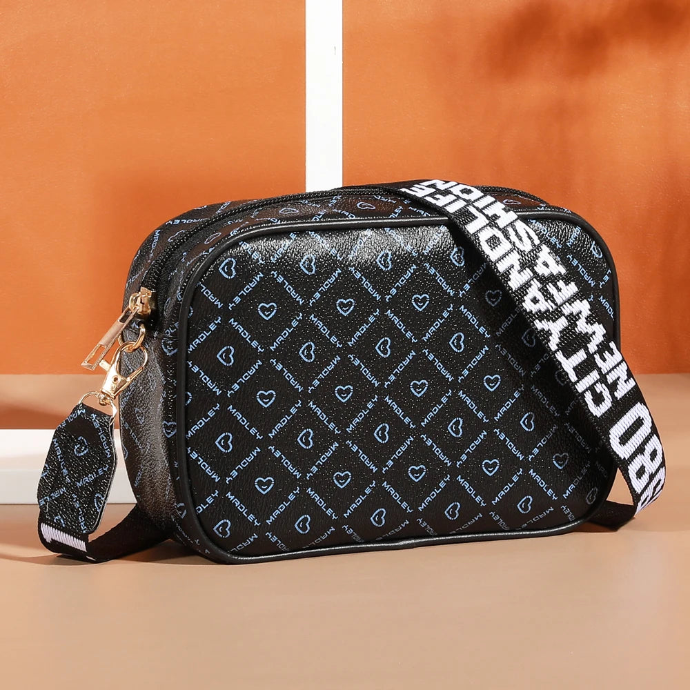 Black compact crossbody bag with a patterned print and gold hardware resting on a light surface.