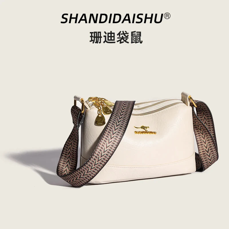 A beige PU leather crossbody shoulder bag with gold hardware and a patterned strap.