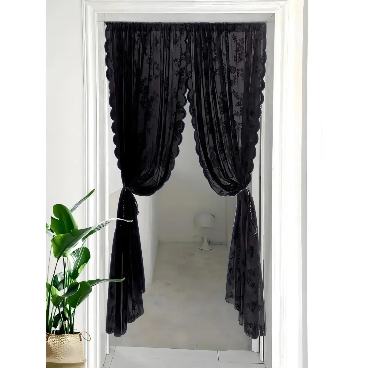 Rideau noir transparent avec broderie florale accroché dans un cadre de porte blanc.
