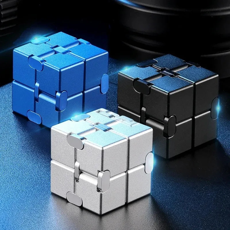 A set of metal infinity fidget cubes in blue, black, and silver resting on a dark surface.
