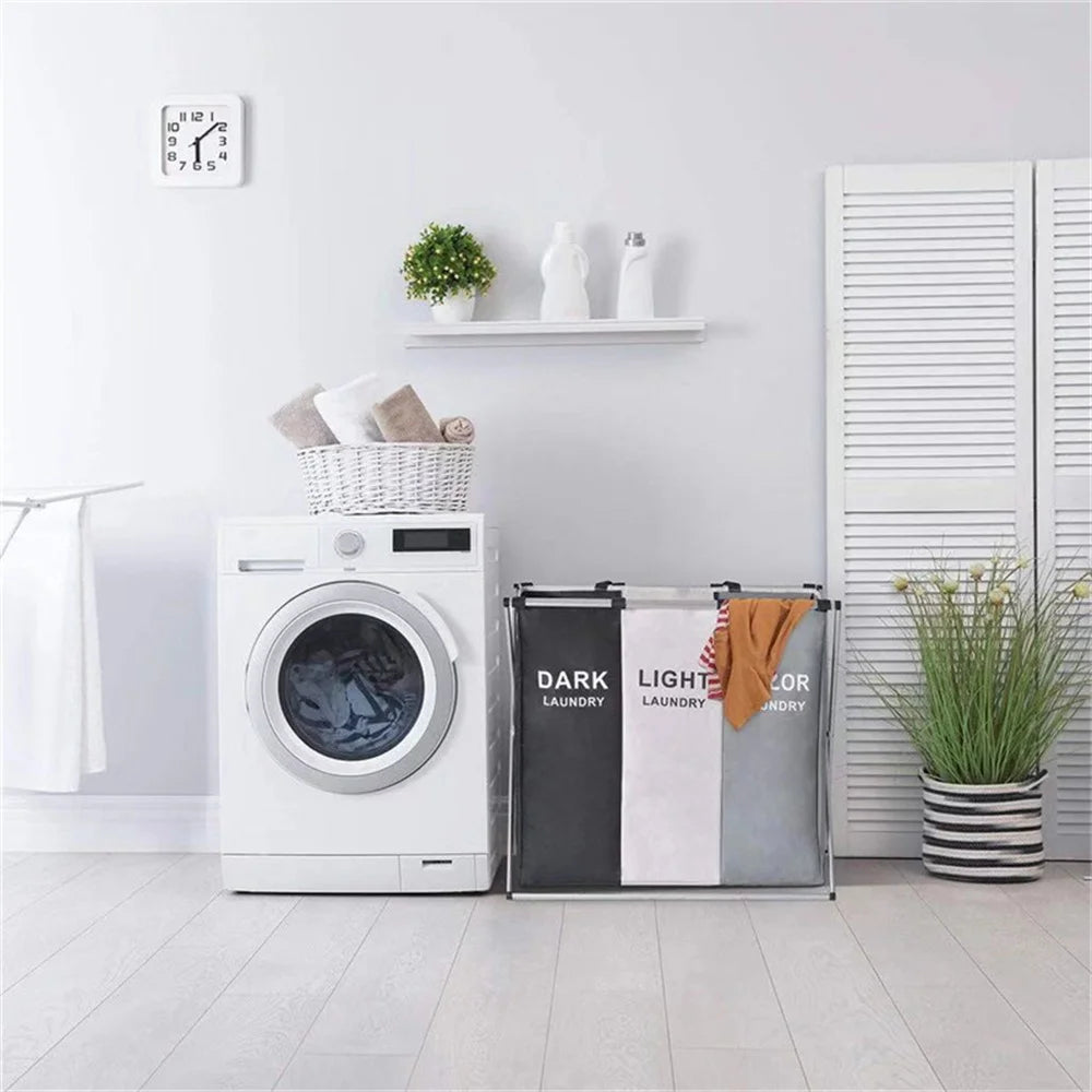 A white foldable laundry basket with handles and sorting compartments sits on a light wood floor.