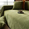 A close-up of a moss green herringbone chenille sofa throw draped over a sofa with orange accent pillows.