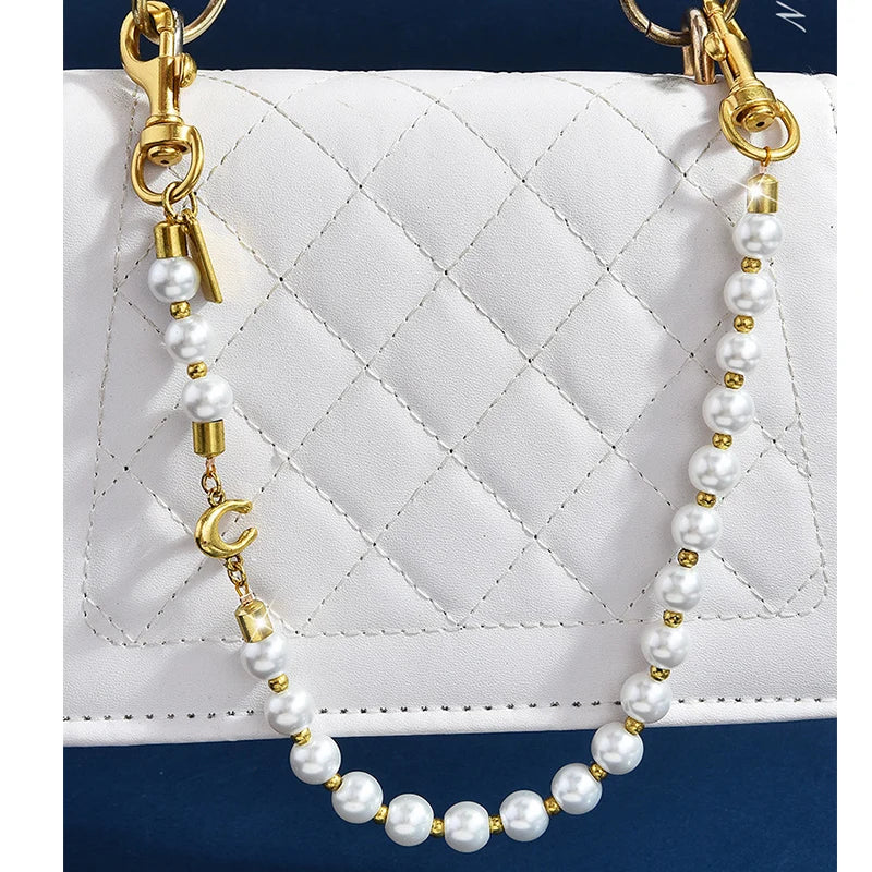 A pearl necklace with a gold letter C charm draped over a white quilted purse.